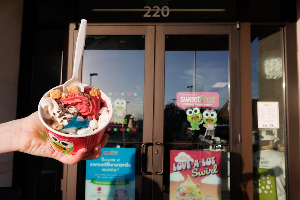 A size small bowl full of frozen yogurt flavors and toppings in front of the entrance door to SweetFrog. 