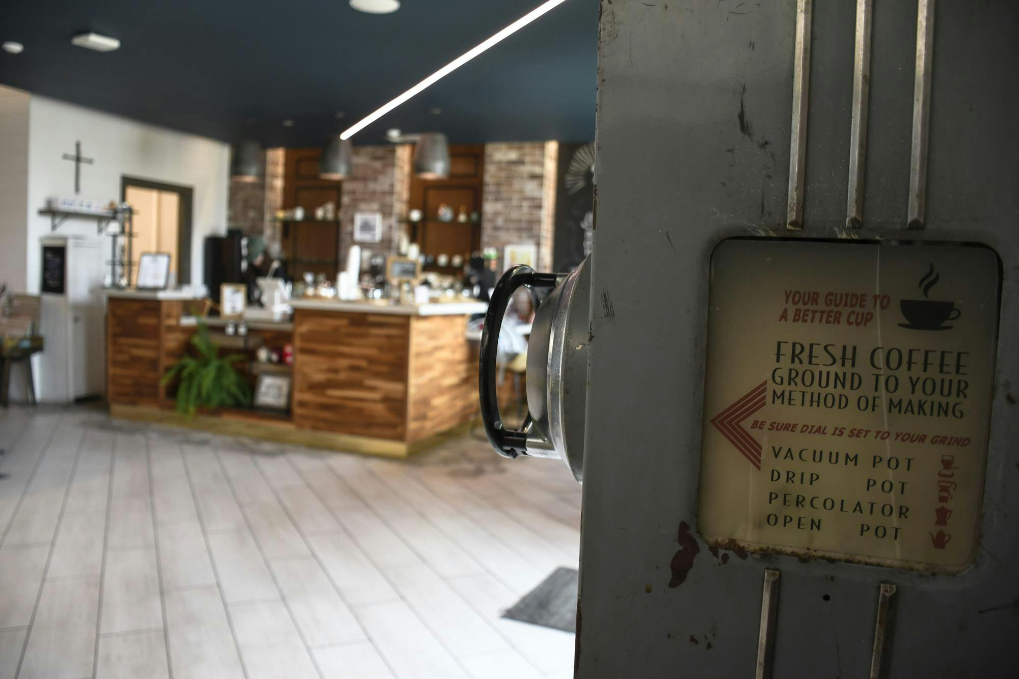 A coffee shop features a wooden counter with various drinks, a menu sign, and a stylish interior with overhead lights.