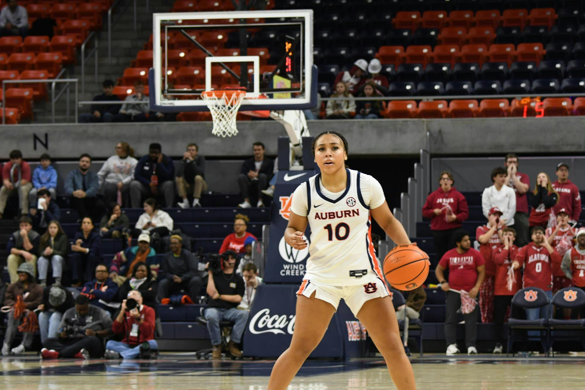 A basketball player in an Auburn uniform dribbles a ball while fans sit in the background, watching the game.