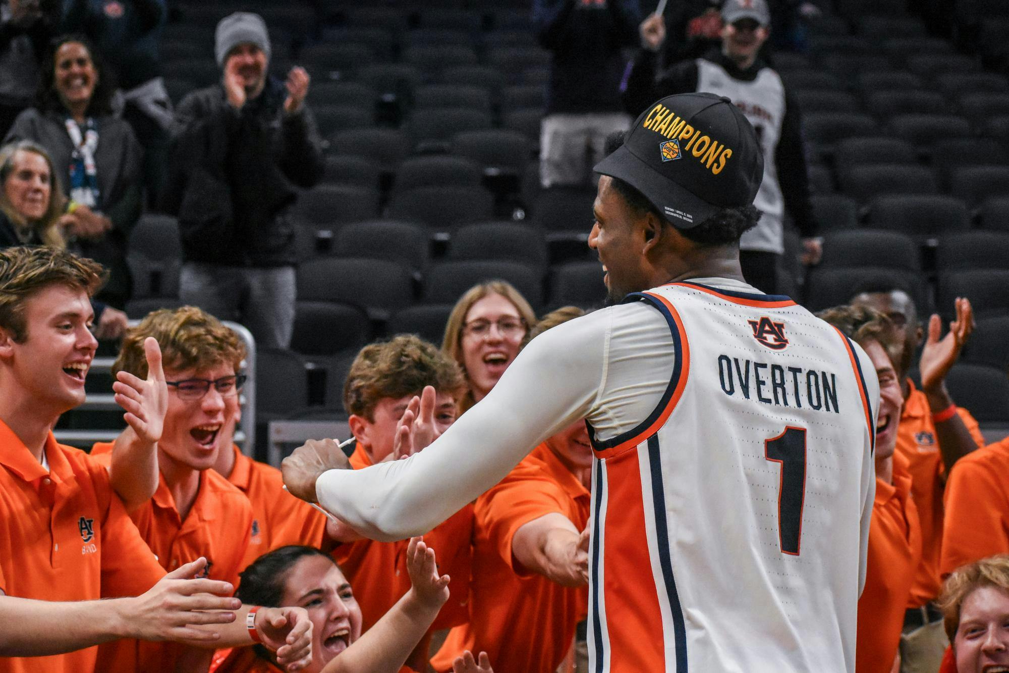 A basketball player in a jersey celebrates with cheering fans wearing orange shirts, all in a sports arena setting.