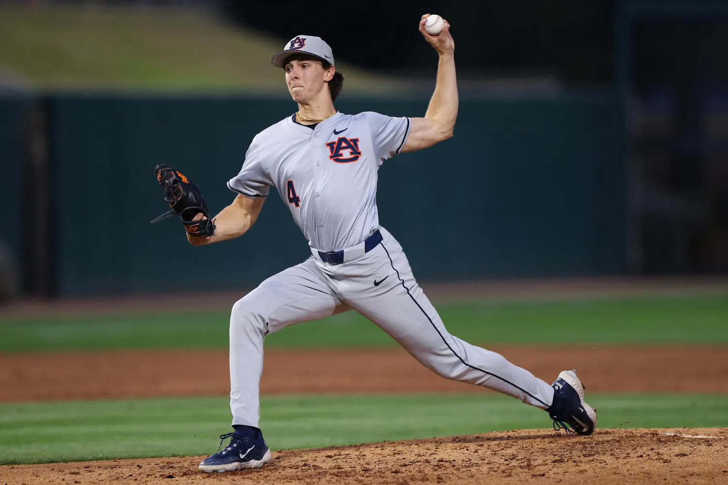 A baseball player in a gray uniform with "Auburn" logo winds up to pitch, holding a ball in his right hand.