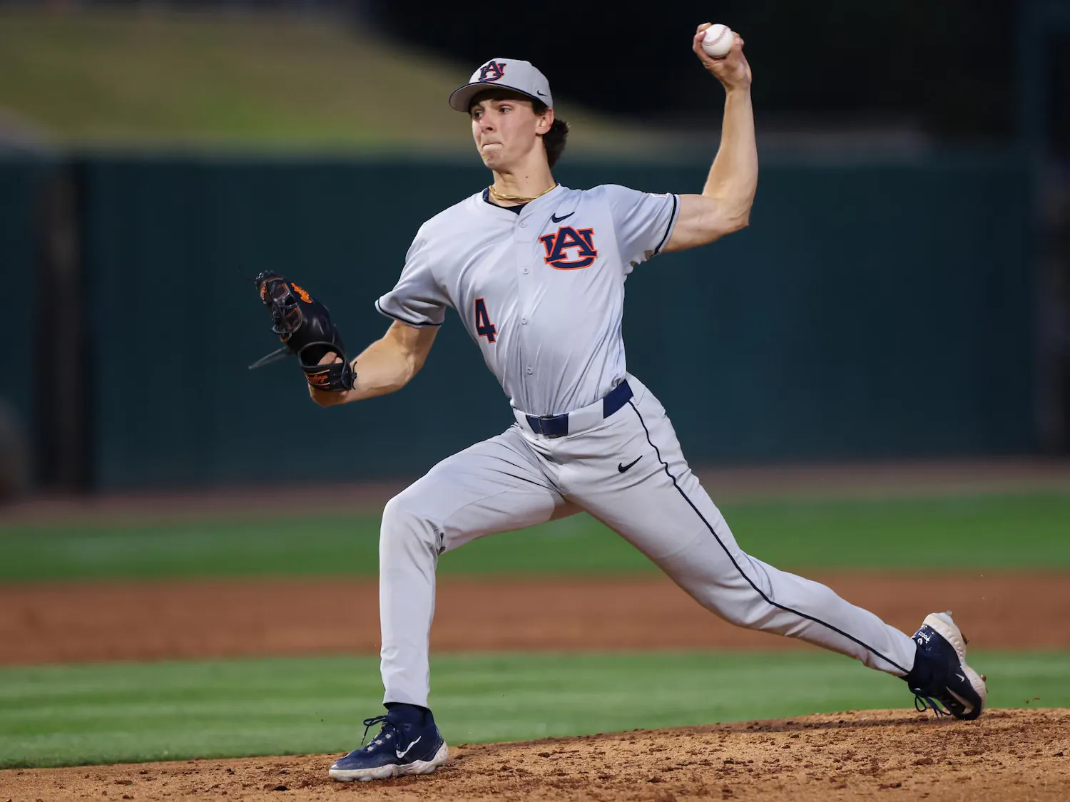 A baseball player in a gray uniform with "Auburn" logo winds up to pitch, holding a ball in his right hand.