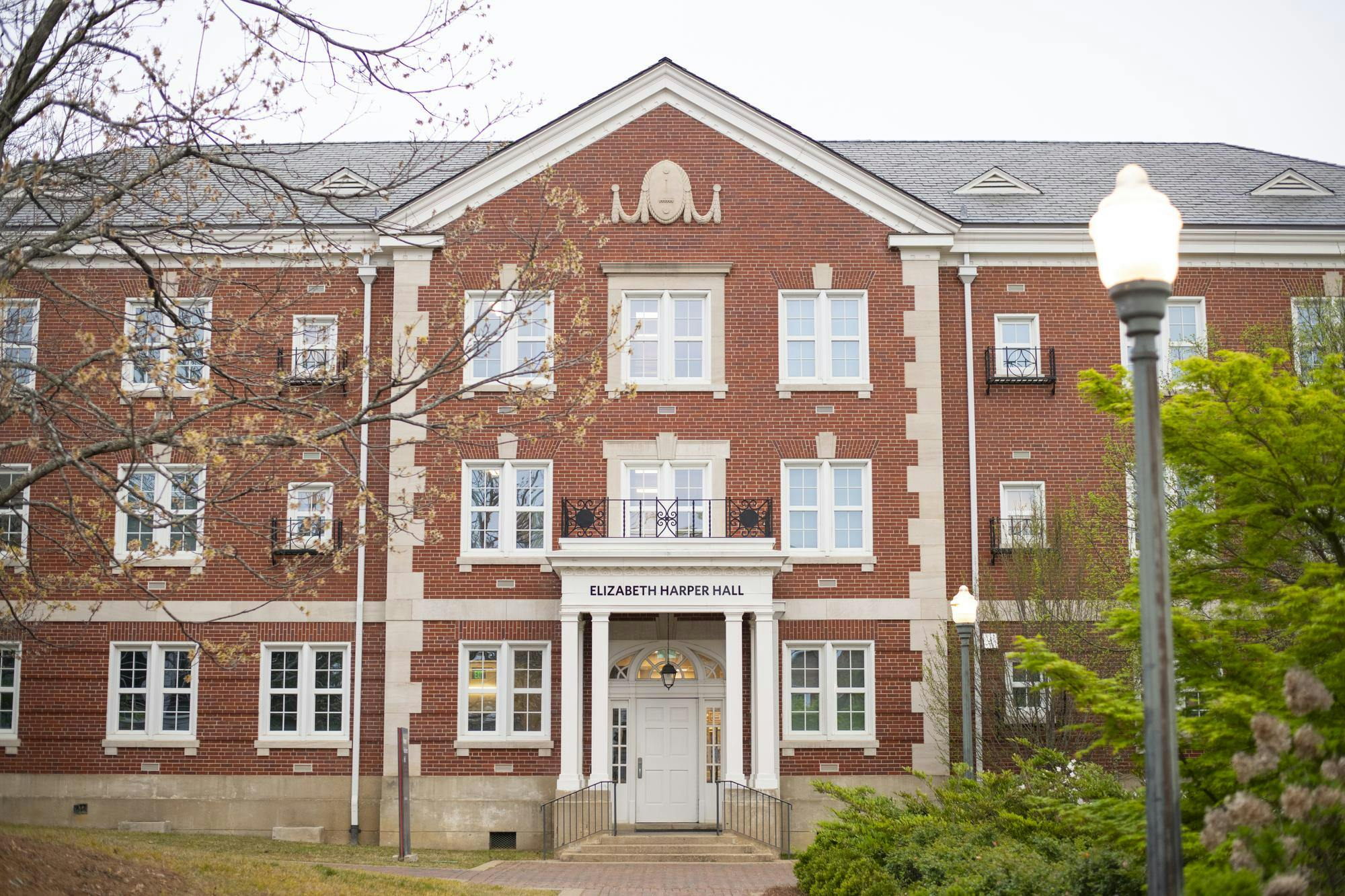 A brick building with multiple windows, a central entrance, and a sign reading "ELIZABETH HARPER HALL" at the front.