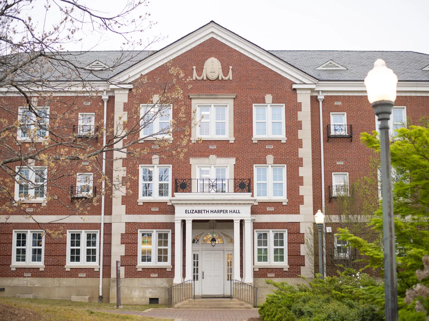 A brick building with multiple windows, a central entrance, and a sign reading "ELIZABETH HARPER HALL" at the front.
