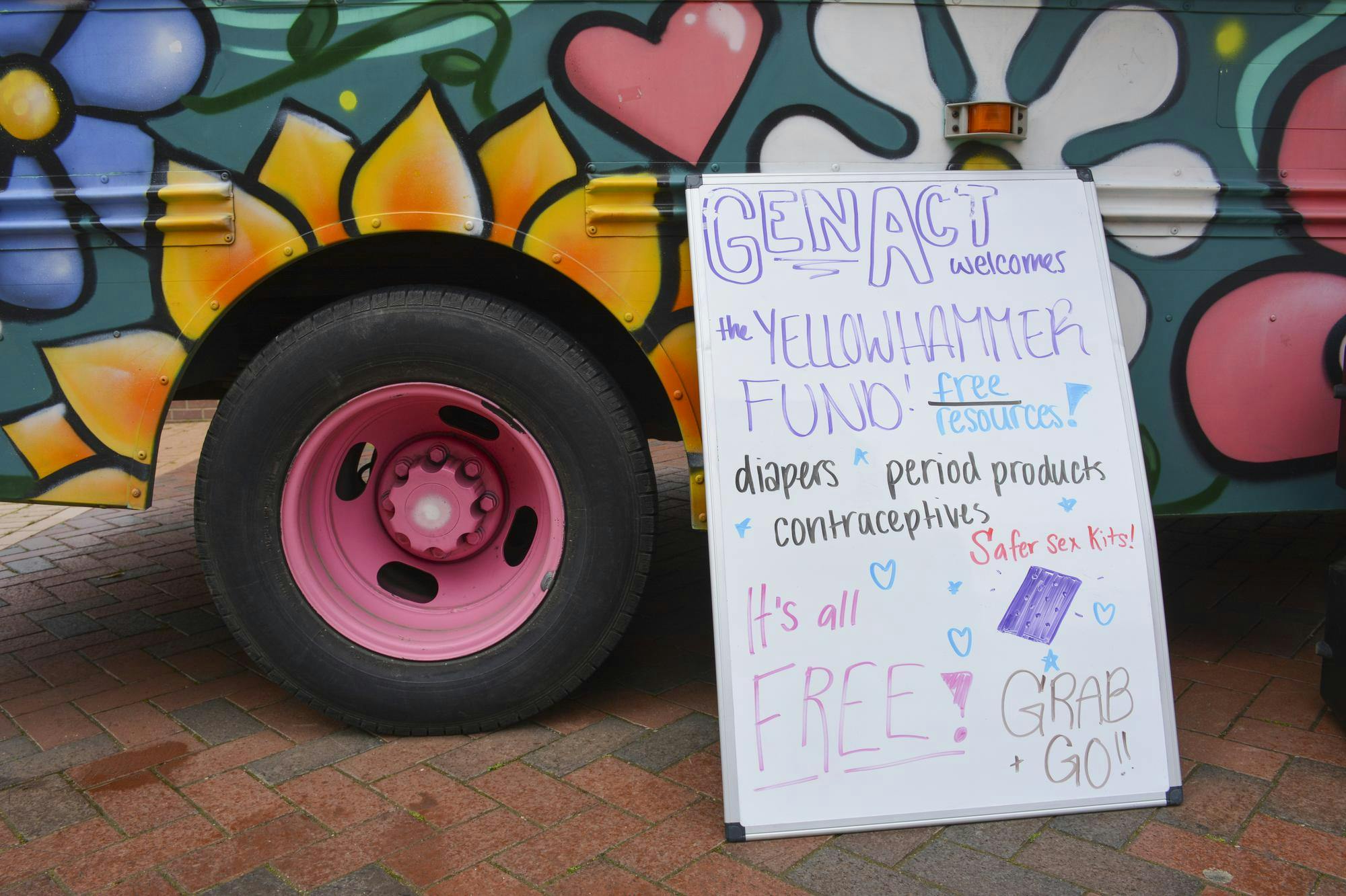 A colorful food truck features vibrant flower murals alongside a sign announcing free resources like diapers and contraceptives.