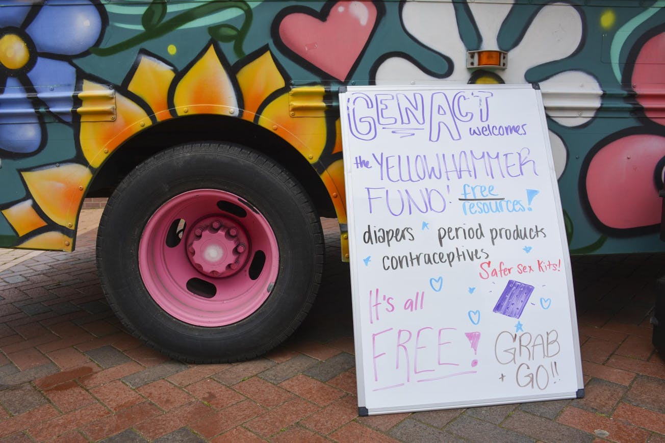 A colorful food truck features vibrant flower murals alongside a sign announcing free resources like diapers and contraceptives.