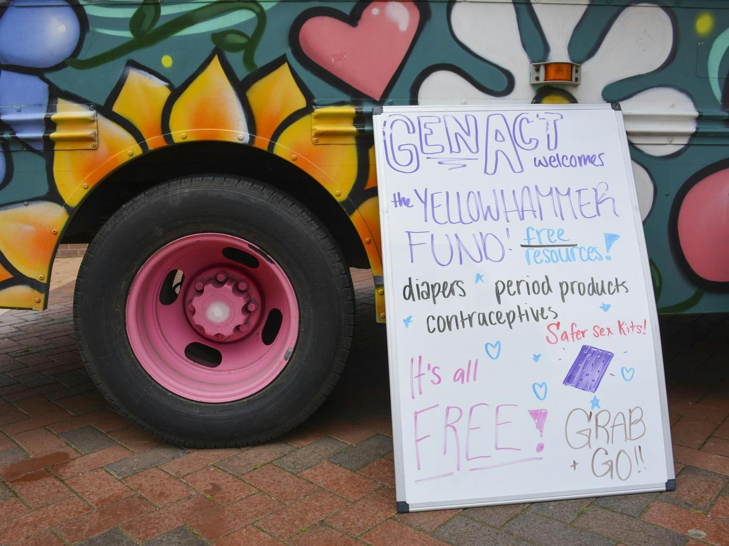 A colorful food truck features vibrant flower murals alongside a sign announcing free resources like diapers and contraceptives.