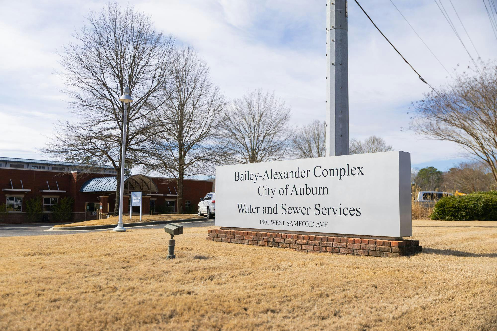 A large sign displays "Bailey-Alexander Complex, City of Auburn, Water and Sewer Services" in front of a brick building and trees.