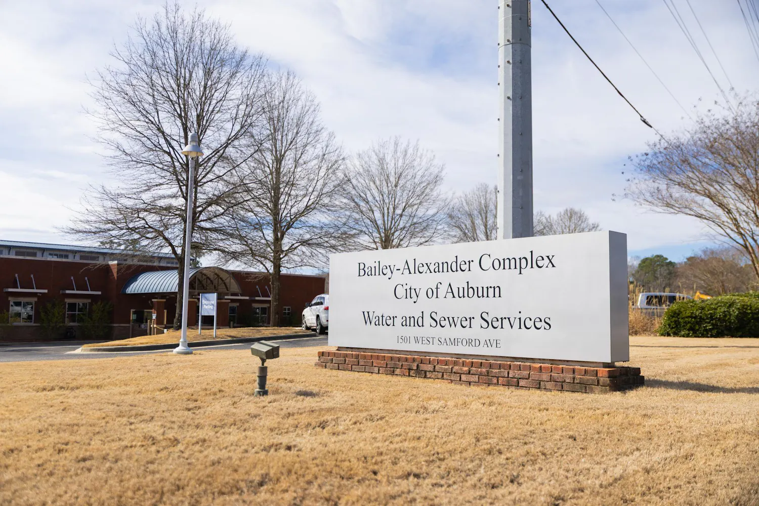A large sign displays "Bailey-Alexander Complex, City of Auburn, Water and Sewer Services" in front of a brick building and trees.