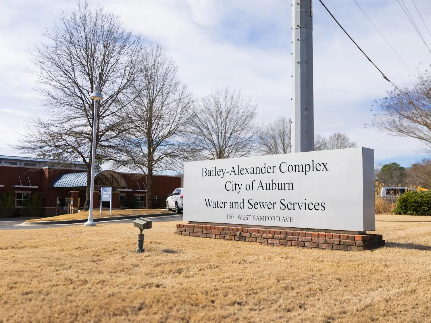 A large sign displays "Bailey-Alexander Complex, City of Auburn, Water and Sewer Services" in front of a brick building and trees.