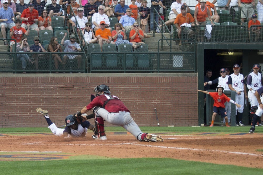 A child in the dugout signals safe after an Auburn baseball player attempts to make it to the home plate. (Jordan Hays | Copy Editor)