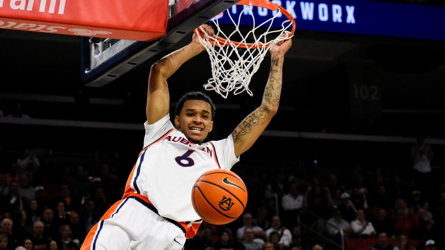 A basketball player hangs from a hoop while preparing to dunk a basketball during a game.