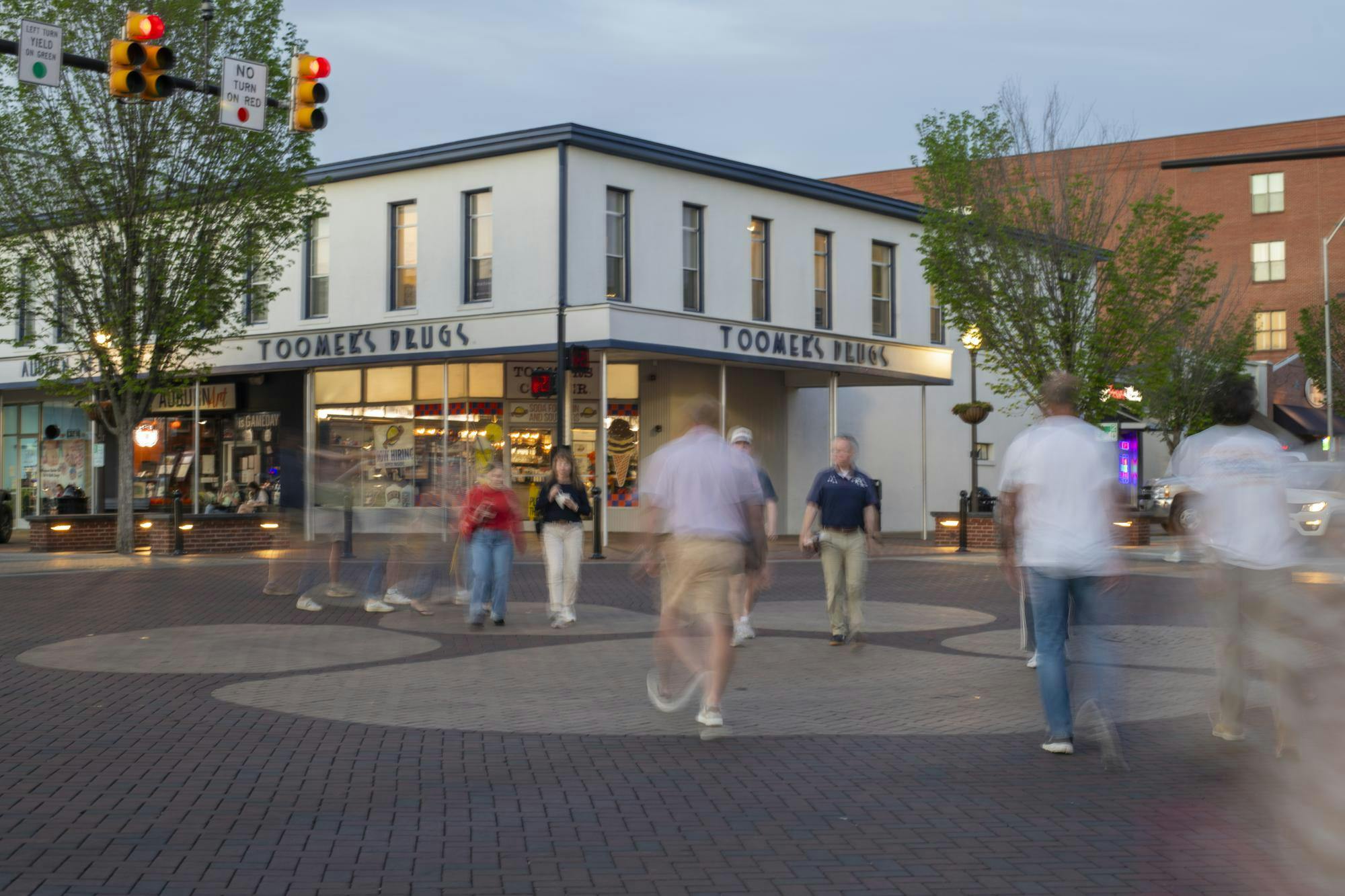 A busy pedestrian area features blurred figures walking past a building with "Toomer's Drugs" signage and illuminated storefronts.