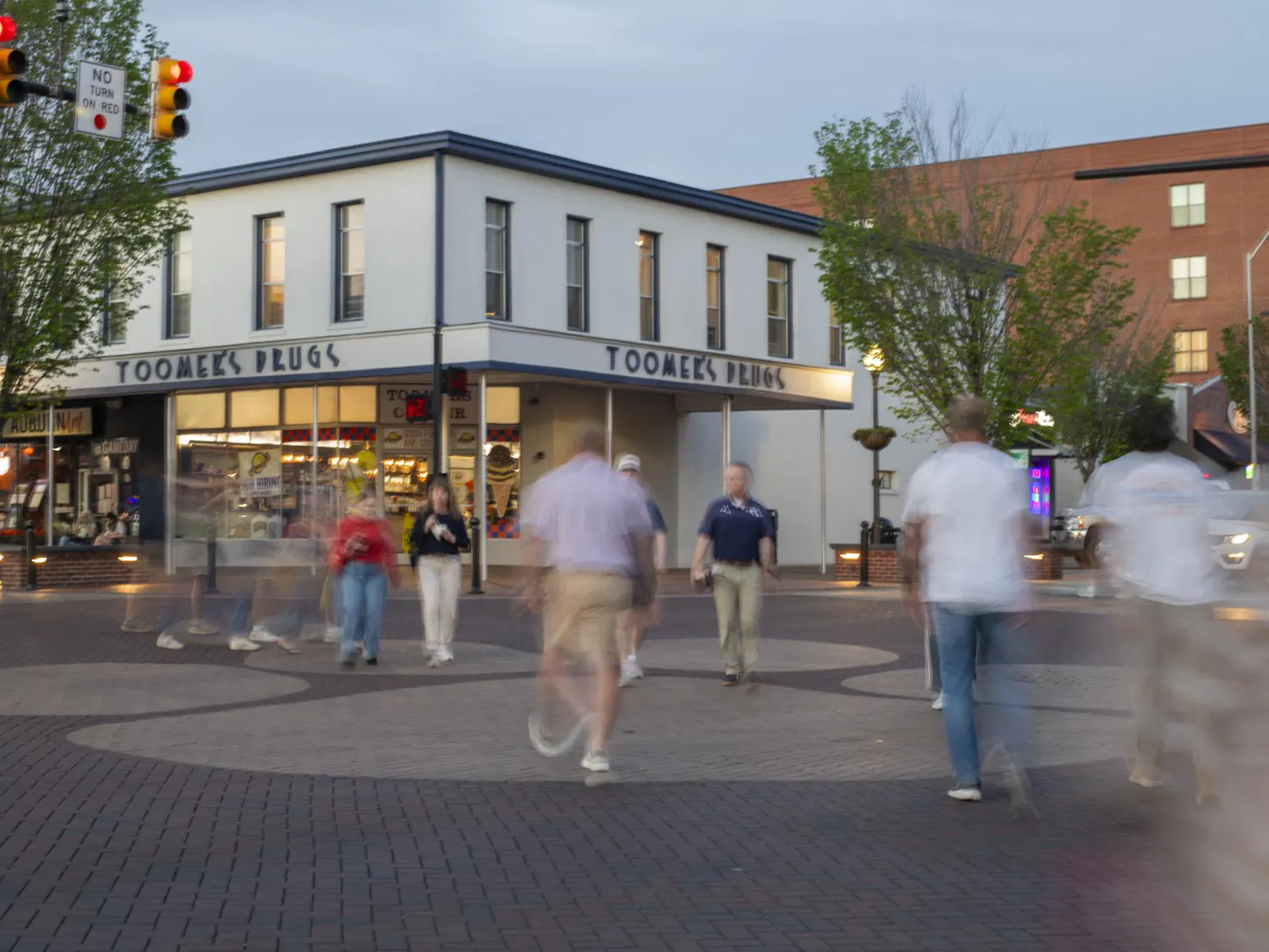 A busy pedestrian area features blurred figures walking past a building with "Toomer's Drugs" signage and illuminated storefronts.
