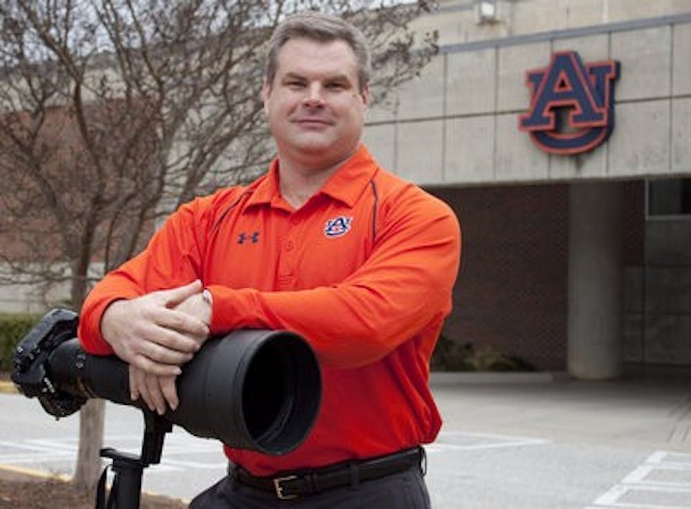 Todd Van Emst, athletic department photographer, stands with his Nikon camera and 400mm lens outside the athletic complex. (Emily Adams/PHOTO EDITOR)