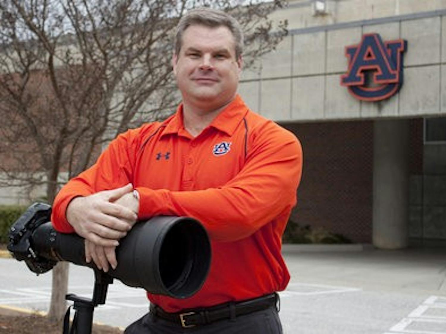 Todd Van Emst, athletic department photographer, stands with his Nikon camera and 400mm lens outside the athletic complex. (Emily Adams/PHOTO EDITOR)