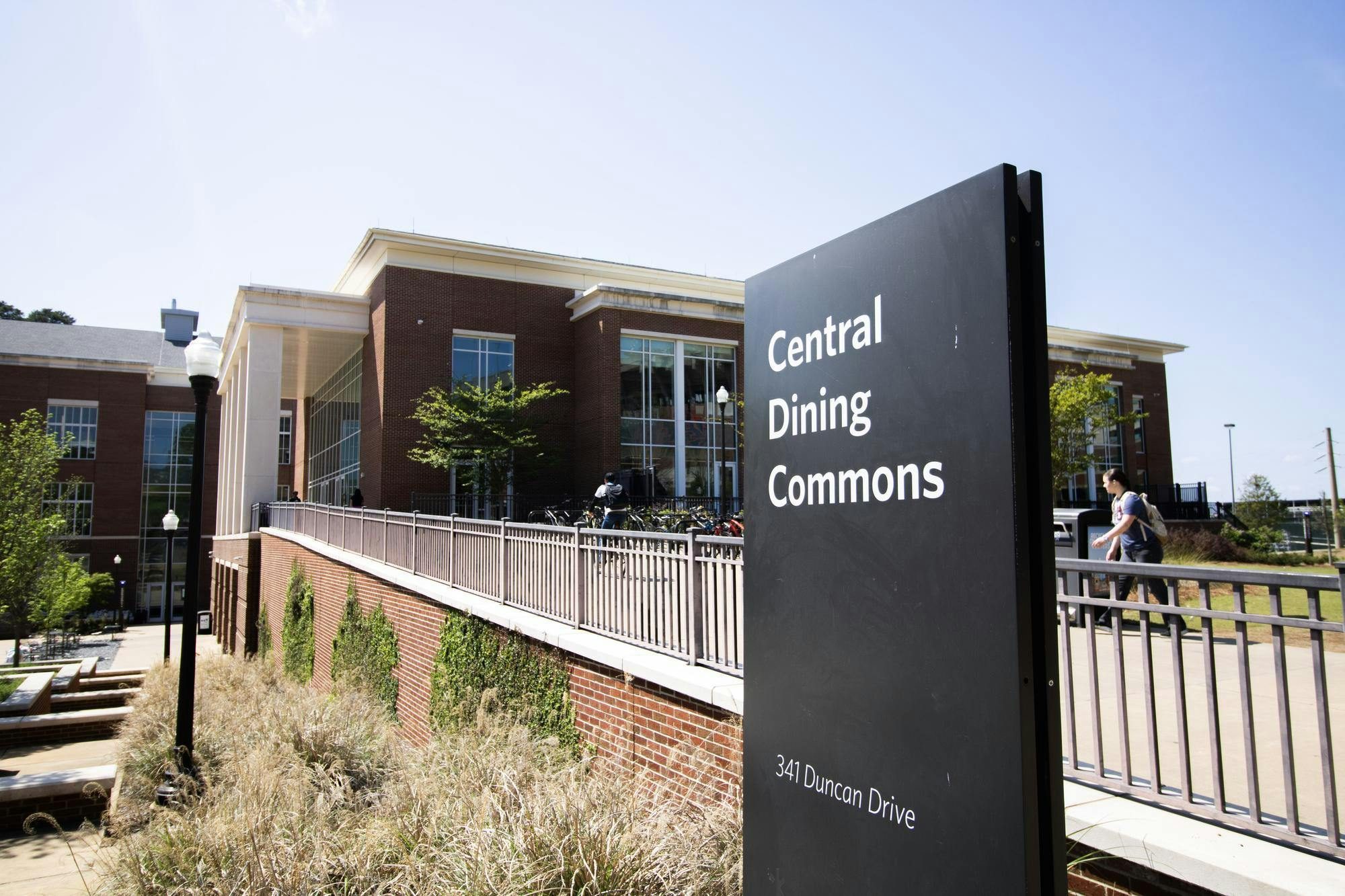 A sign labeled "Central Dining Commons" is positioned near a modern building with glass windows and surrounding greenery.