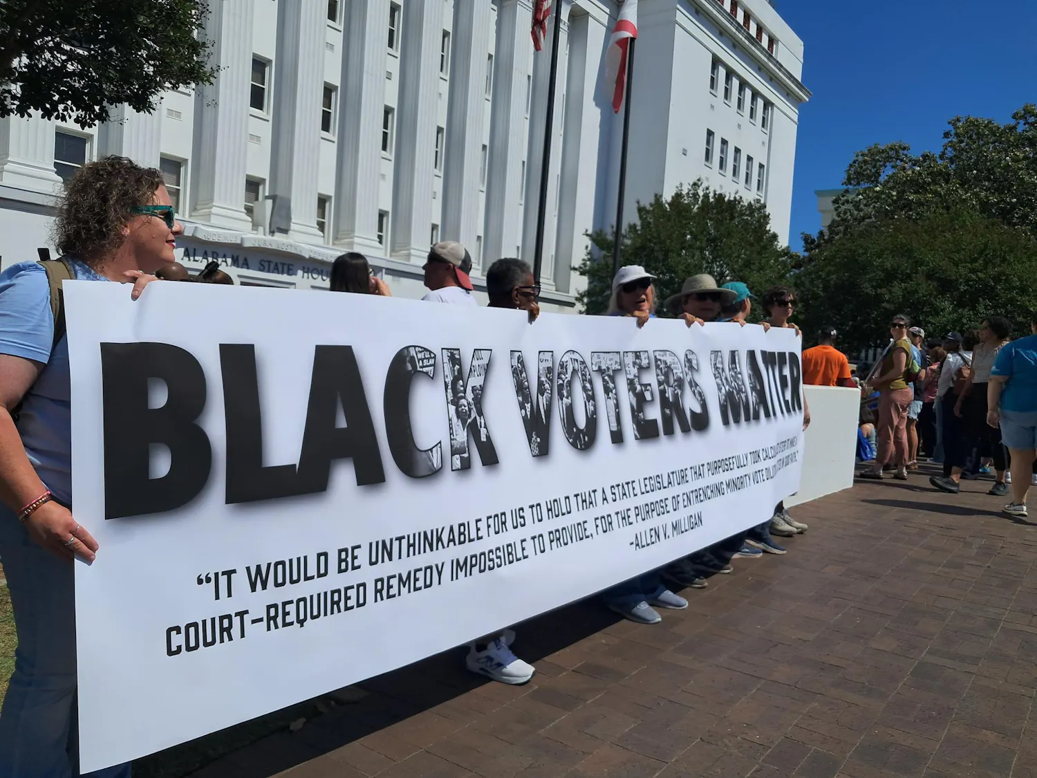 Protesters stand outside the Alabama State House and hold a sign reading “Black Voters Matter” with a quote from the Allen v. Milligan case under it.