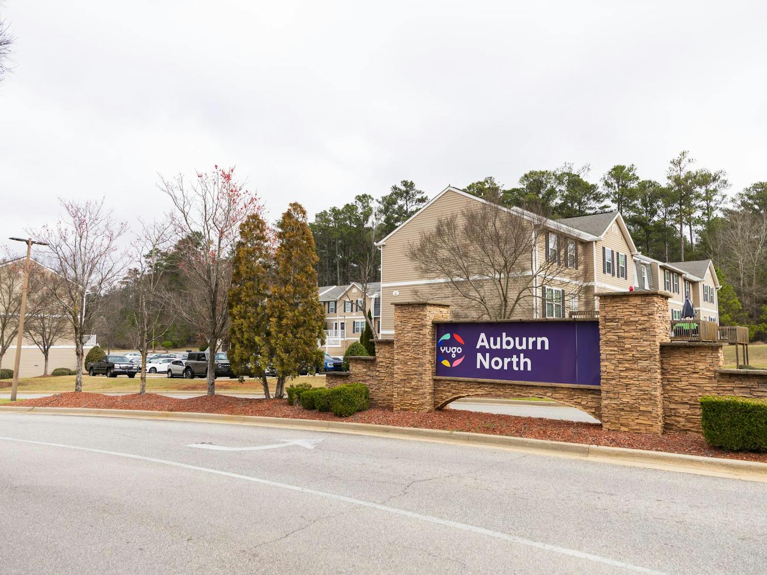 A stone sign displays "Auburn North," flanked by trees and modern apartment buildings under a cloudy sky.