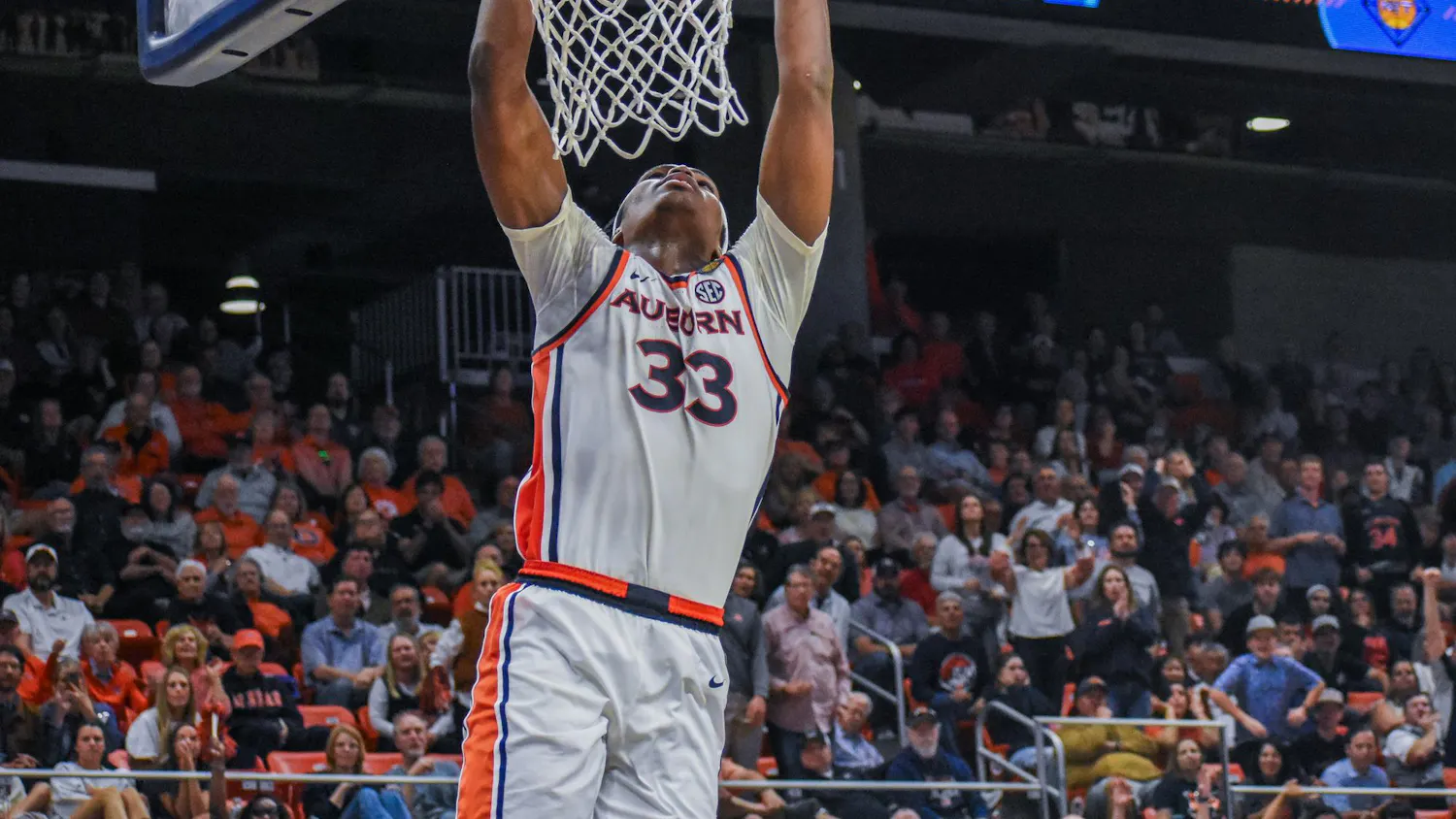 A basketball player in a white uniform with orange and blue accents is performing a dunk into the hoop.