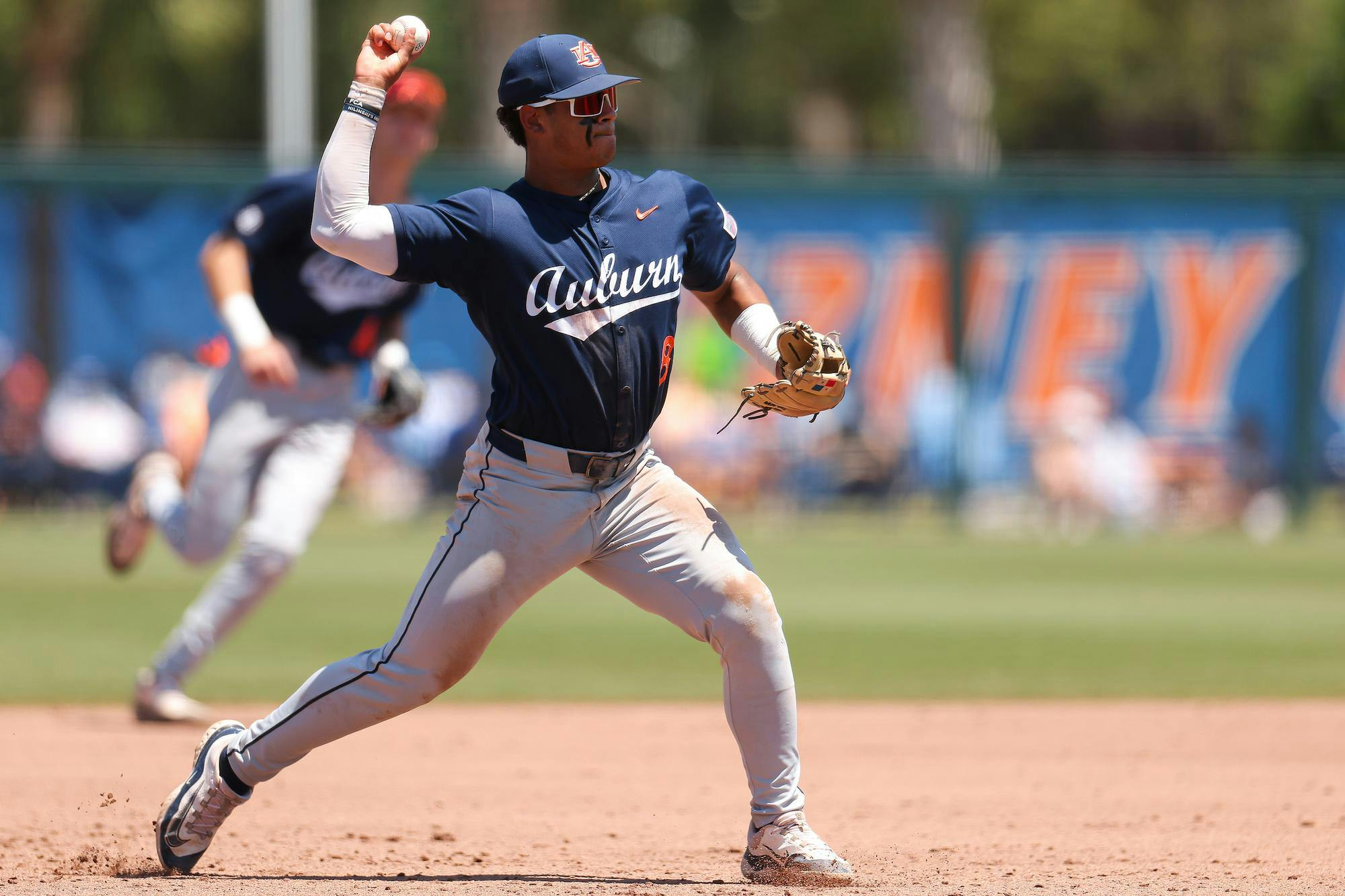 A player in a navy uniform prepares to throw a baseball, with dirt smudges on his pants and a focused expression.