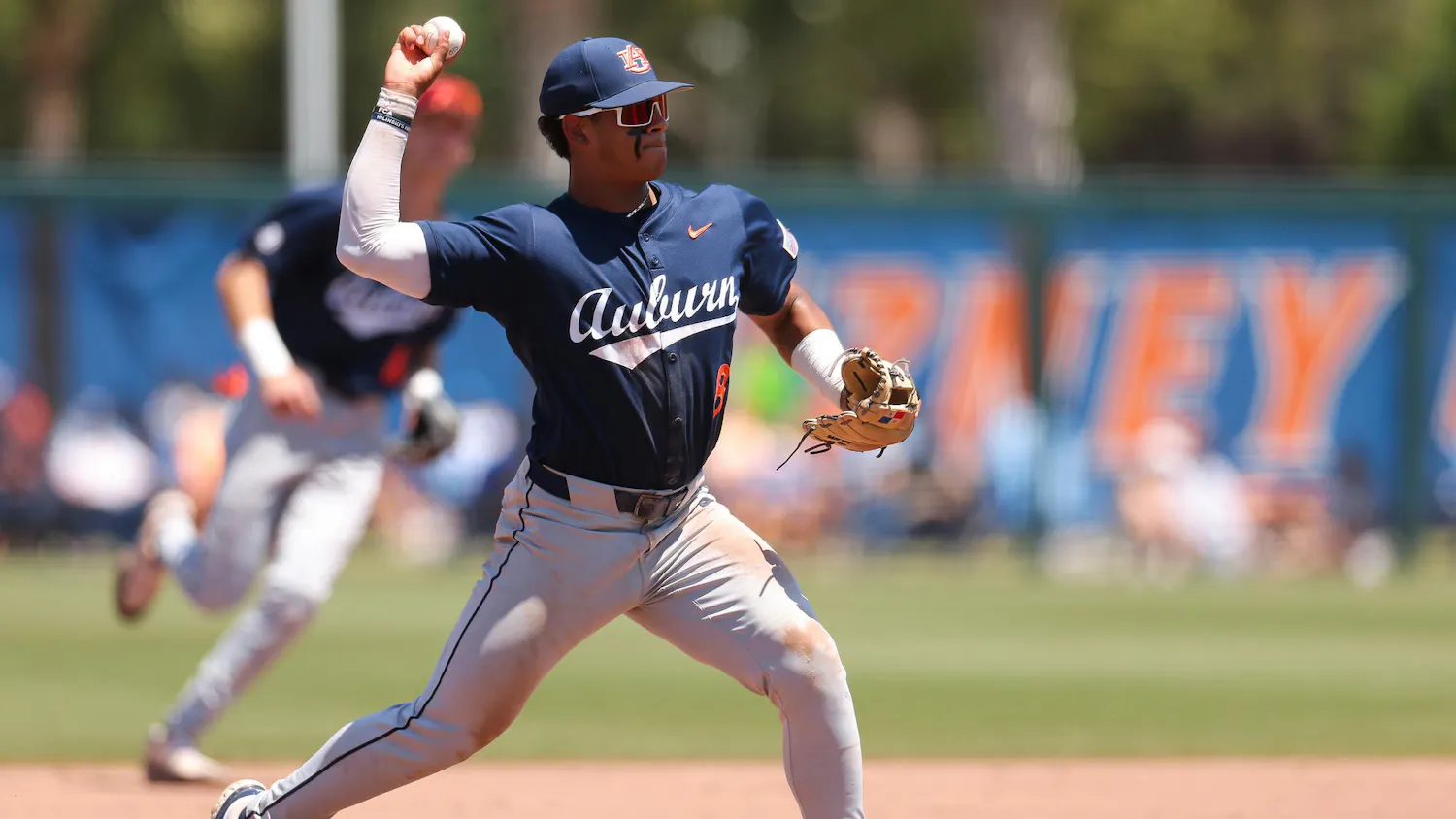 A player in a navy uniform prepares to throw a baseball, with dirt smudges on his pants and a focused expression.