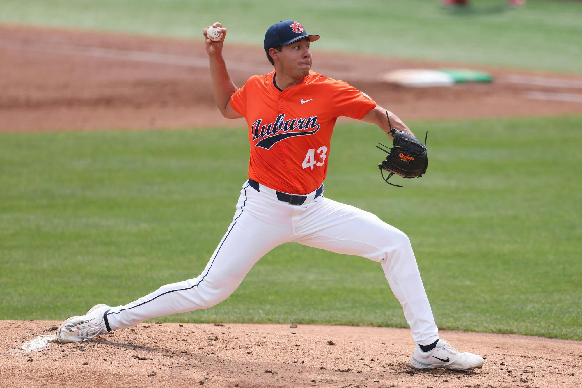 A baseball pitcher, wearing an orange jersey and white pants, prepares to throw a ball on a grassy field.