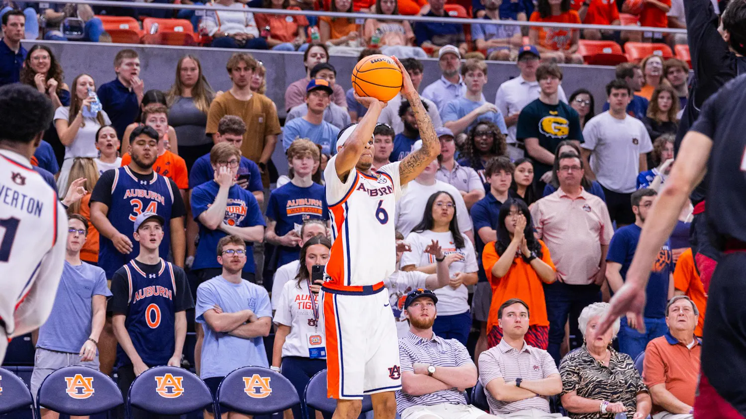 A basketball player in a white uniform prepares to shoot while a lively crowd in the background cheers and reacts.