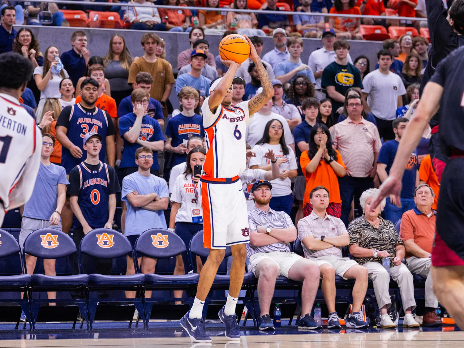 A basketball player in a white uniform prepares to shoot while a lively crowd in the background cheers and reacts.