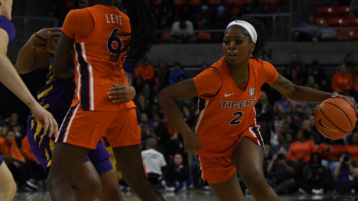 Two female basketball players are engaged in a competitive play, one dribbling a basketball while wearing an orange uniform.
