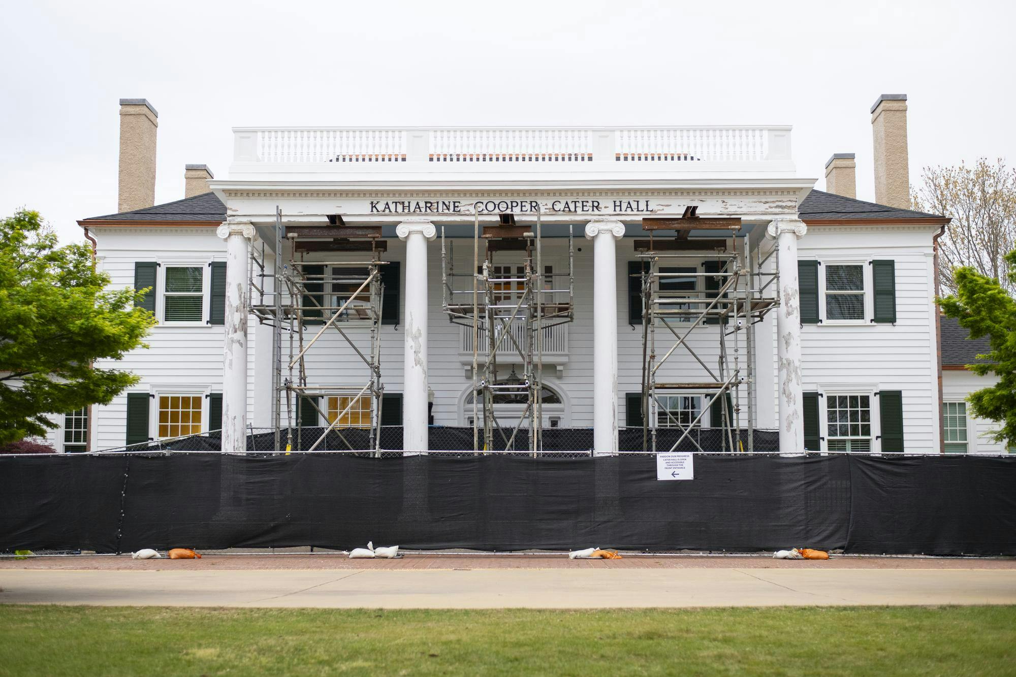 A white, two-story building with green shutters and scaffolding in front, surrounded by a black fence.