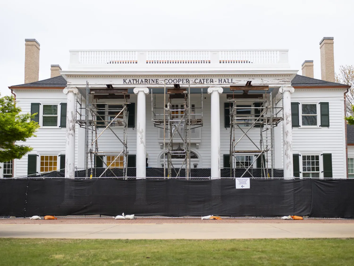 A white, two-story building with green shutters and scaffolding in front, surrounded by a black fence.