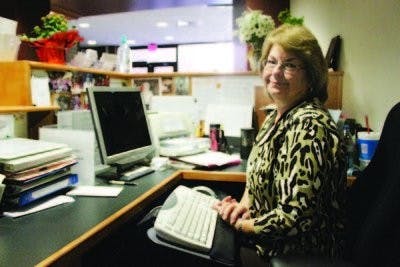 Carolyn Campbell, receptionist of Harrison School of Pharmacy, sits at her desk, where she greets passing pharmacy students with love and candy and takes care of all office needs. (Emily Adams / Photo Editor)