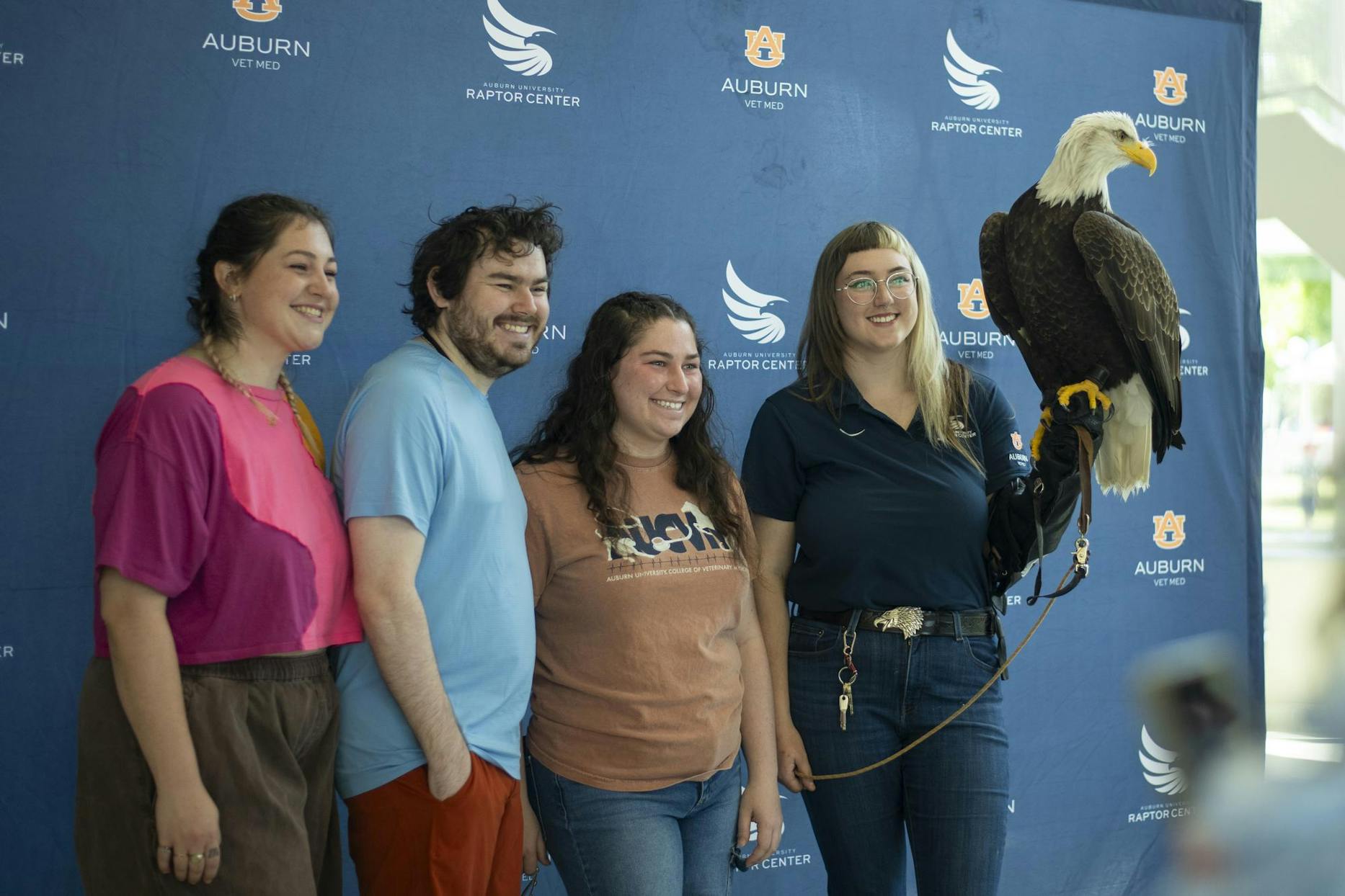 Four people pose together in front of a blue backdrop, with a large eagle perched on one person's arm.