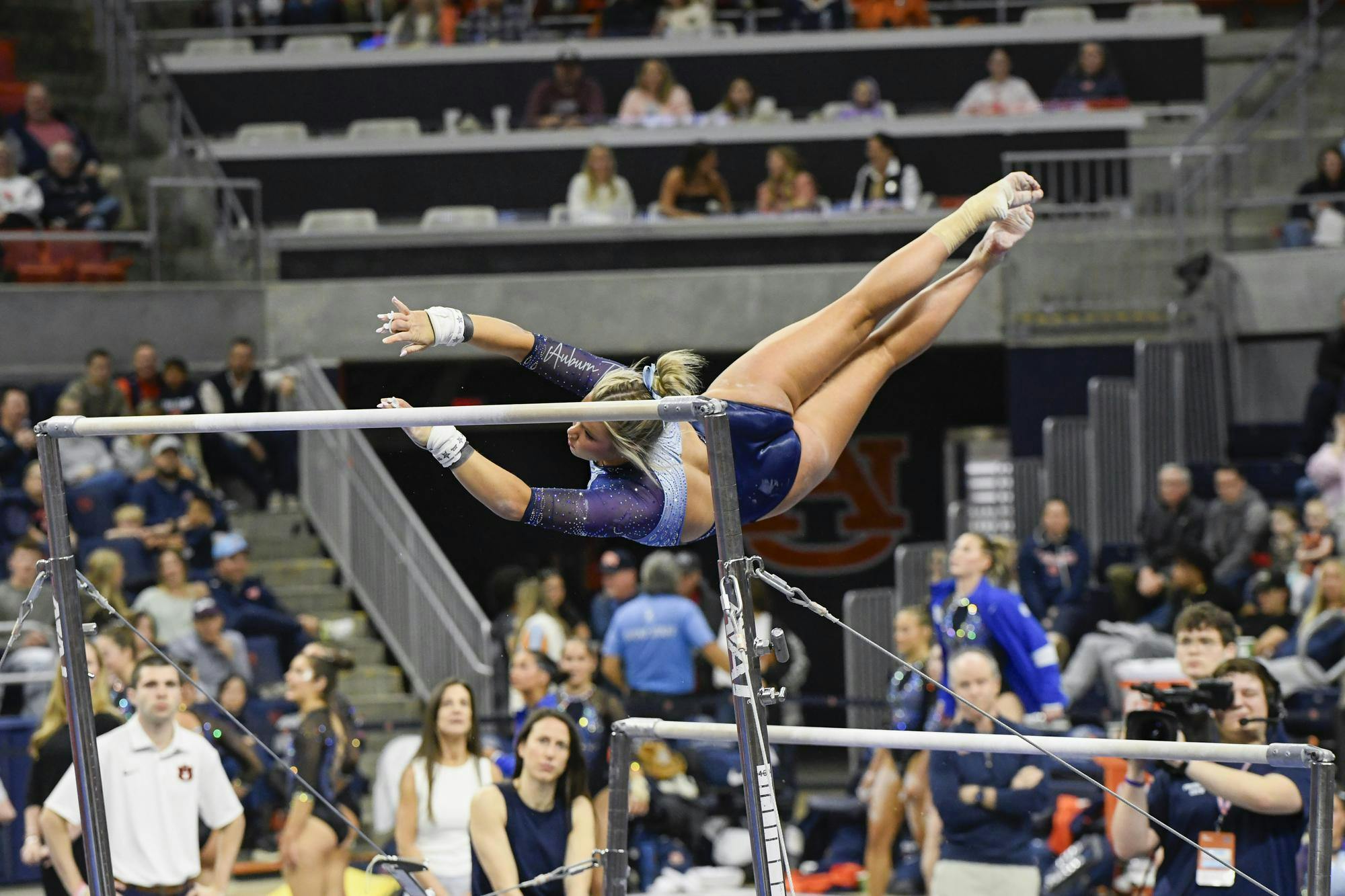 A gymnast executes a dynamic move on uneven bars, surrounded by an audience of captivated spectators.