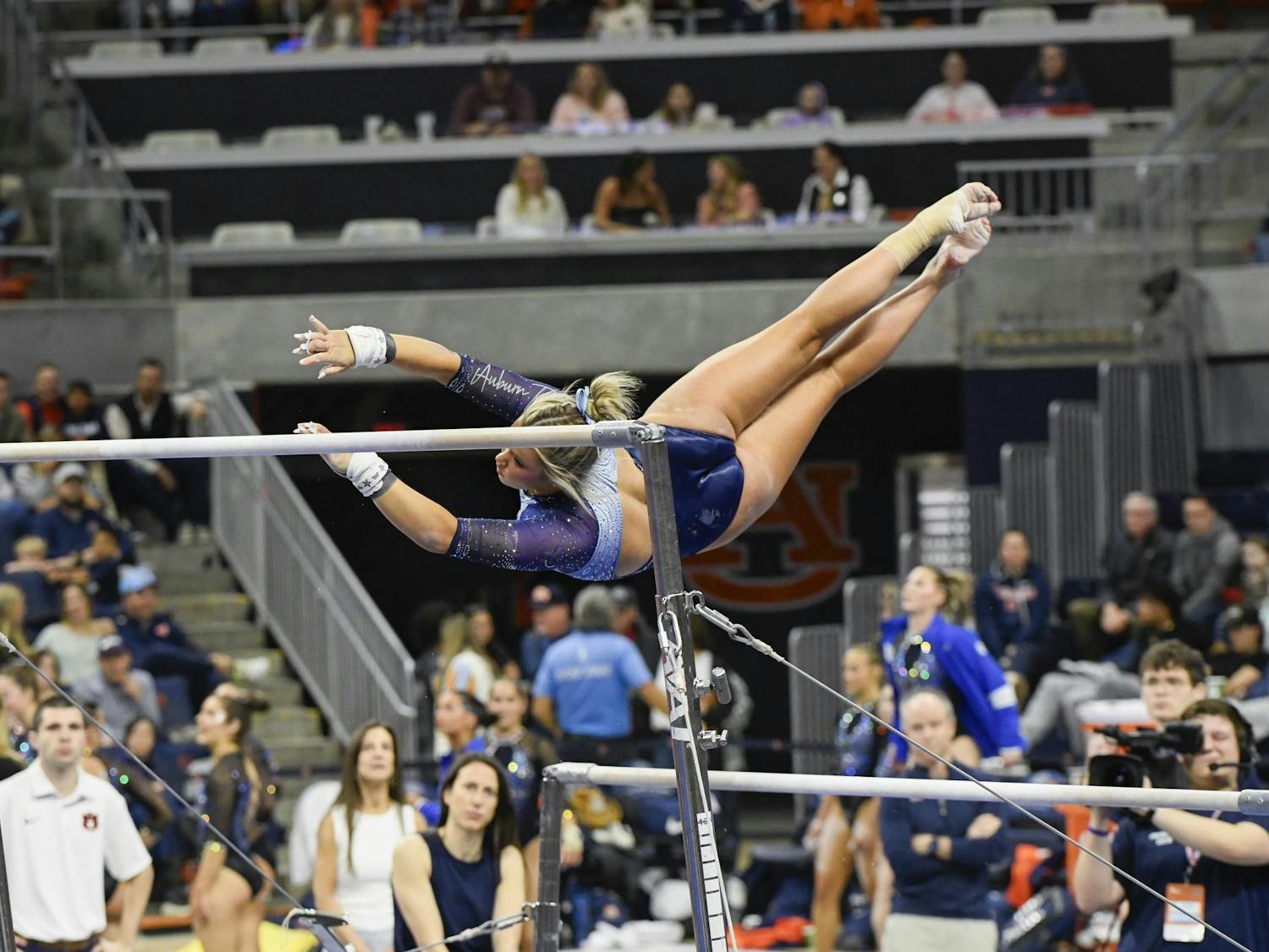 A gymnast executes a dynamic move on uneven bars, surrounded by an audience of captivated spectators.