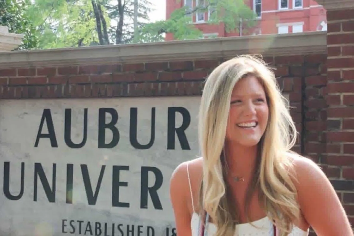 A smiling young woman with long hair stands in front of a large sign that reads "AUBURN UNIVERSITY."