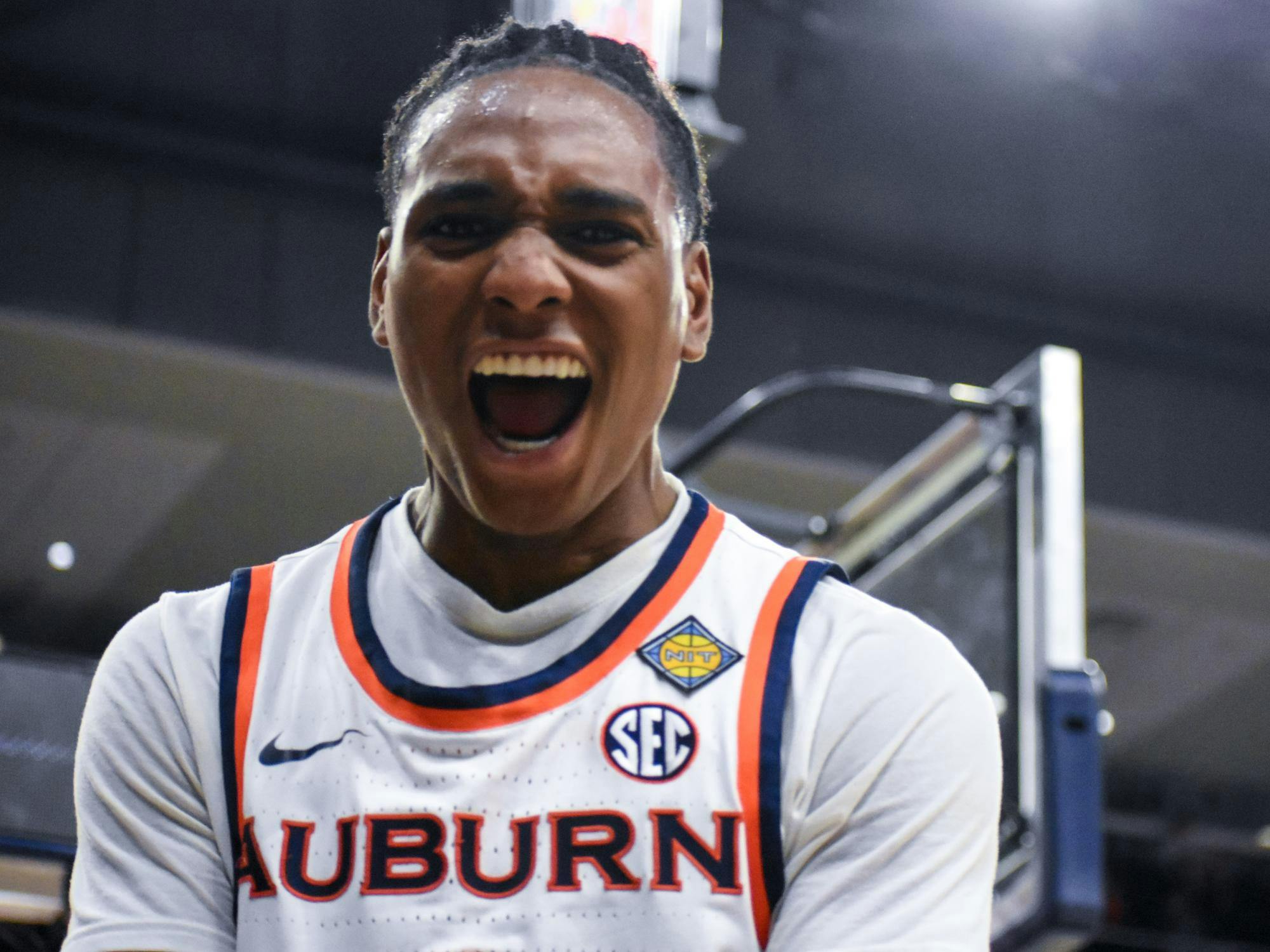 A basketball player in a white jersey with orange and blue accents is celebrating and yelling passionately on the court.
