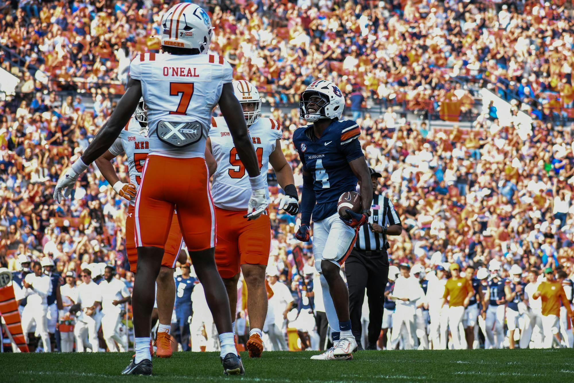 A football player in a dark jersey celebrates while holding a ball, surrounded by teammates and a cheering crowd.