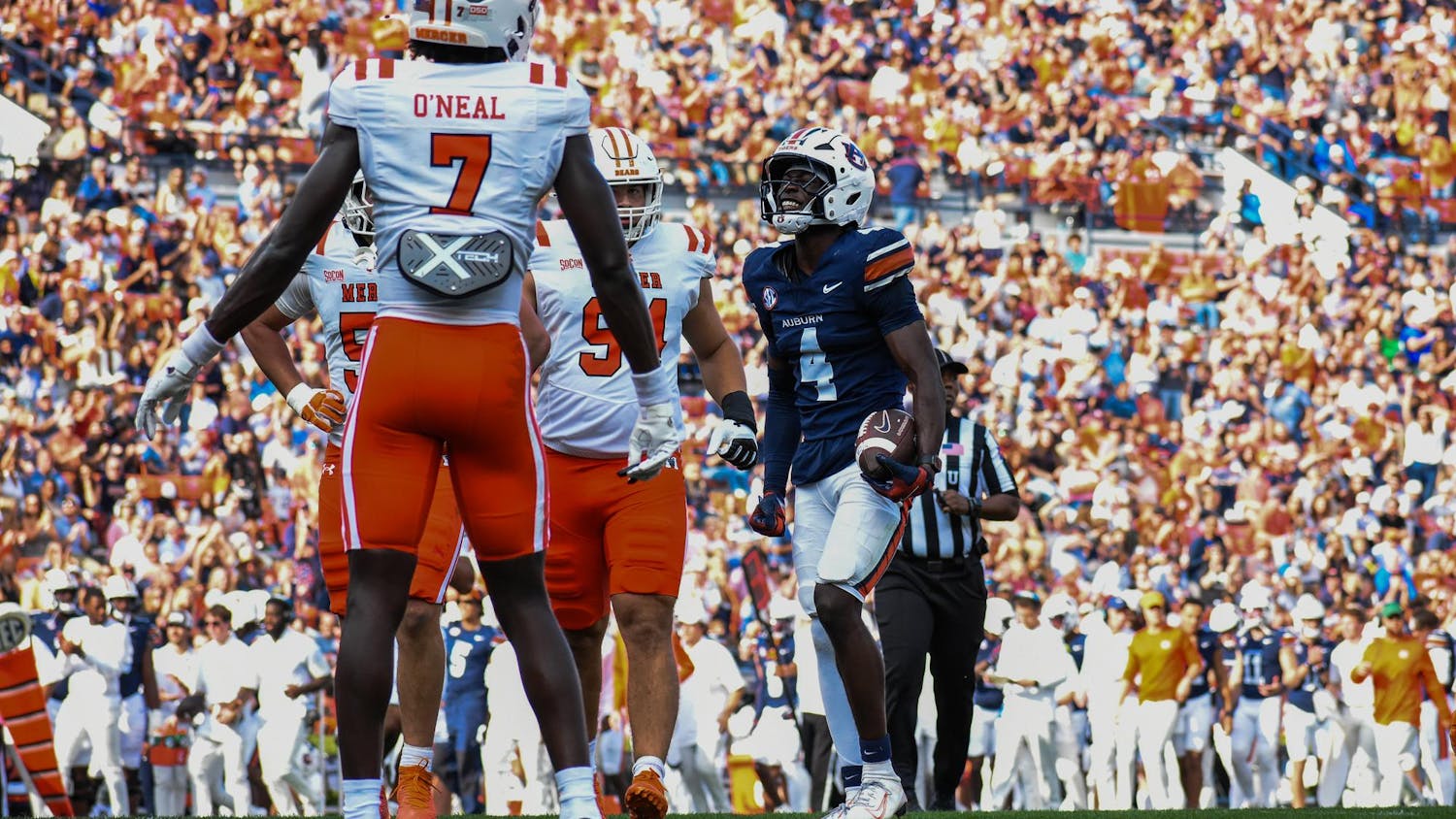 A football player in a dark jersey celebrates while holding a ball, surrounded by teammates and a cheering crowd.