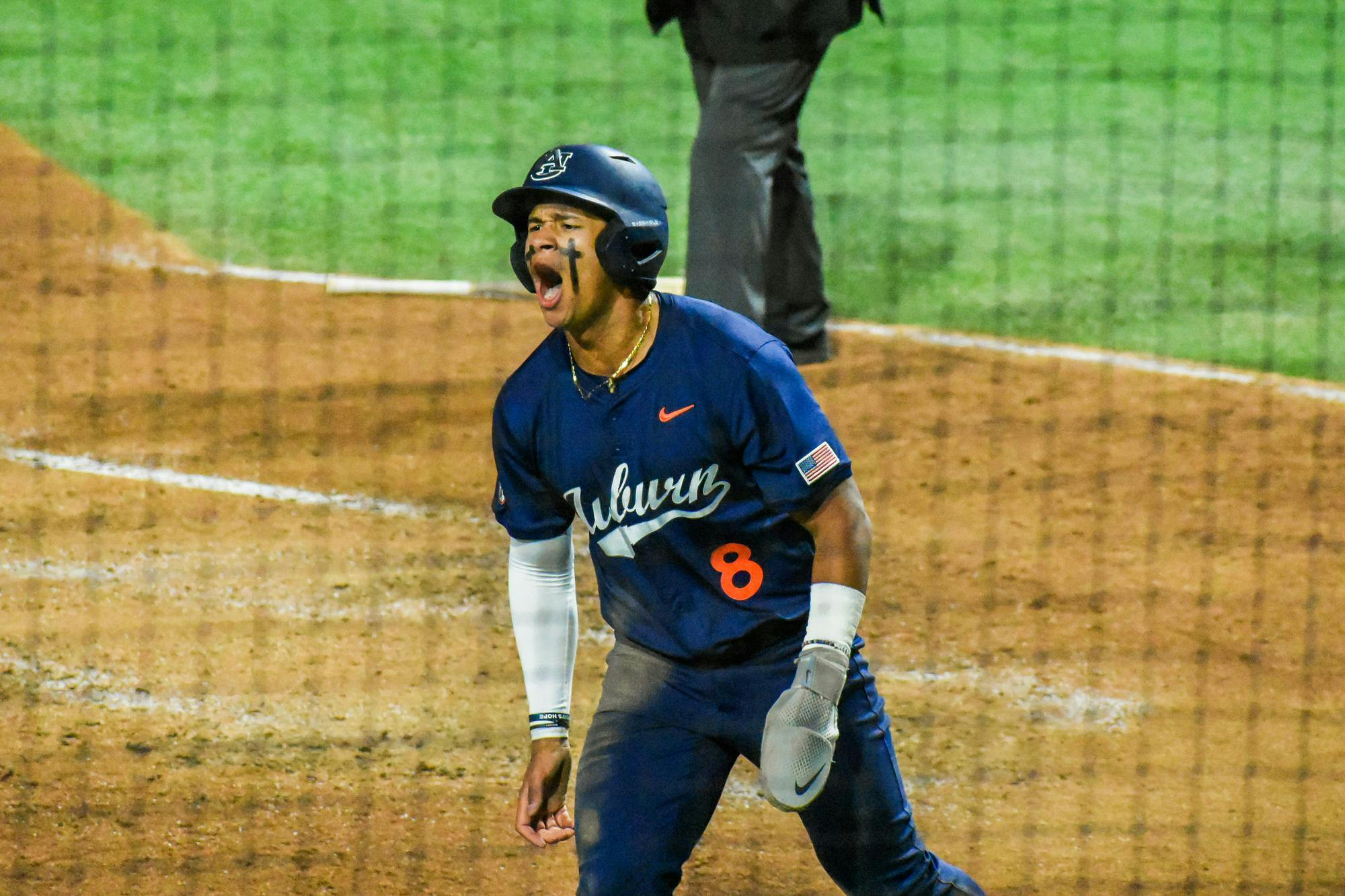 A baseball player in a navy jersey with "Auburn" on it celebrates enthusiastically while standing on a dirt field.