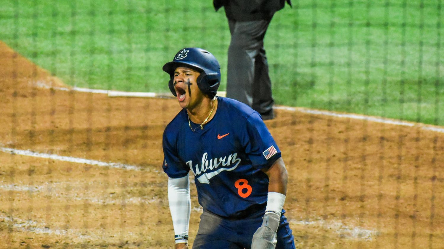 A baseball player in a navy jersey with "Auburn" on it celebrates enthusiastically while standing on a dirt field.