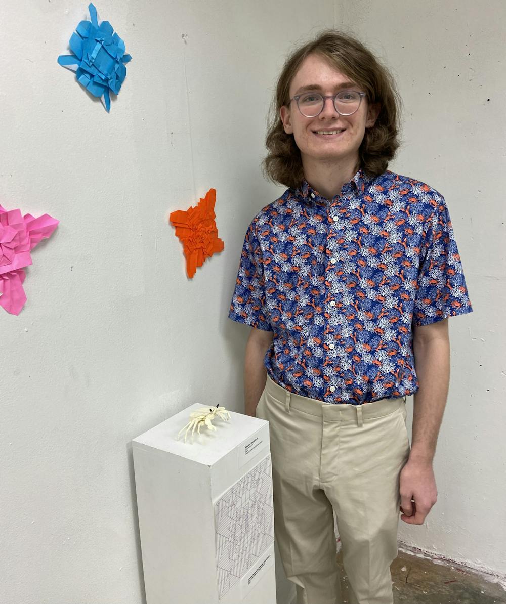 <p>Origami enthusiast Collin Crowder stands proudly next to his design on display in Biggin Hall.</p>