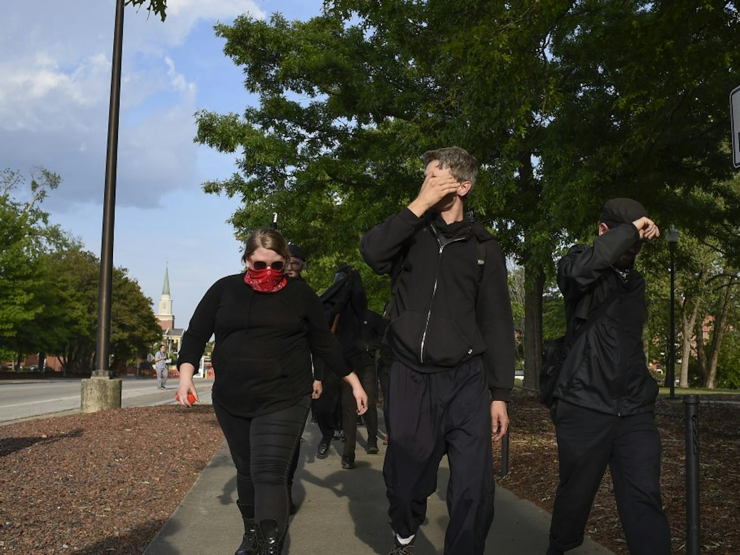 Members of an anti-fascist movement shield their faces after being asked to remove their masks by police, while walking toward Foy Hall on Tuesday, April 18, 2017 in Auburn, Ala. 