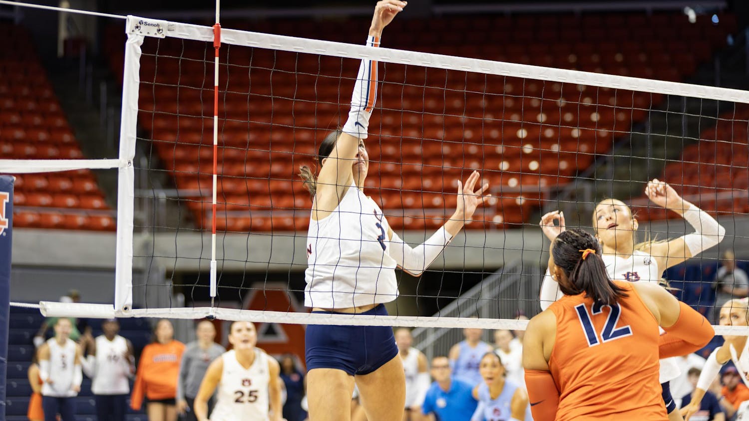 A player leaps to hit a volleyball over a net, with teammates and opponents positioned nearby.