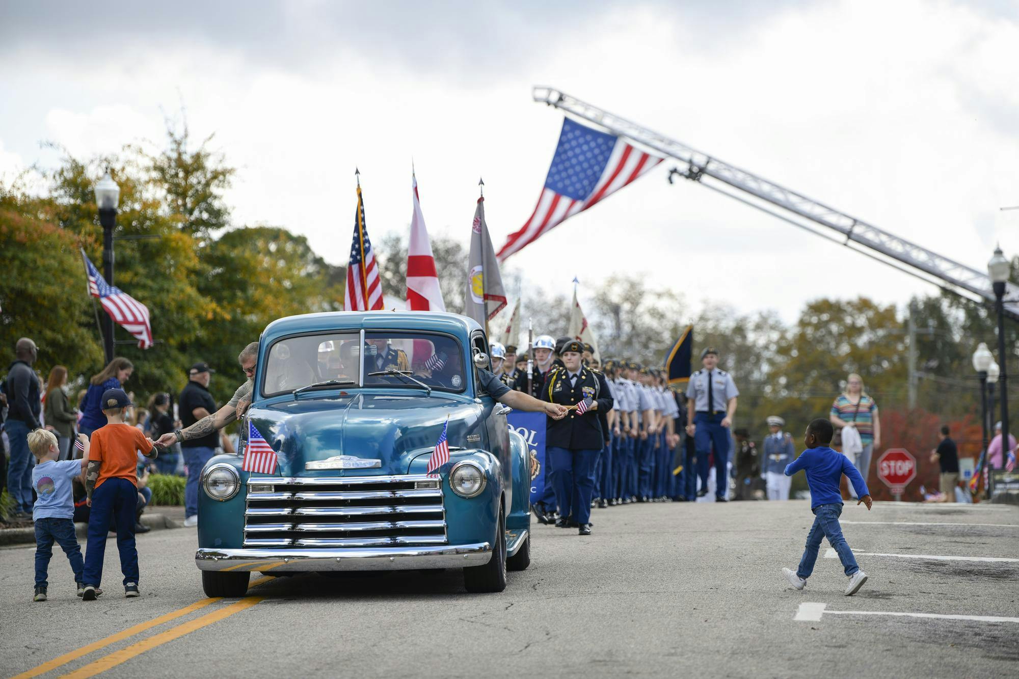 Children run to collect flags from a vintage car during the Freedom Fest Veterans Parade in Opelika, Ala., on Saturday, Nov. 8, 2025.