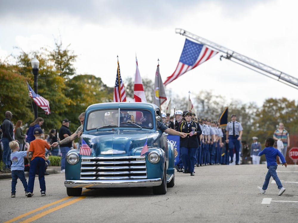 Children run to collect flags from a vintage car during the Freedom Fest Veterans Parade in Opelika, AL on Saturday, Nov. 8, 2025.