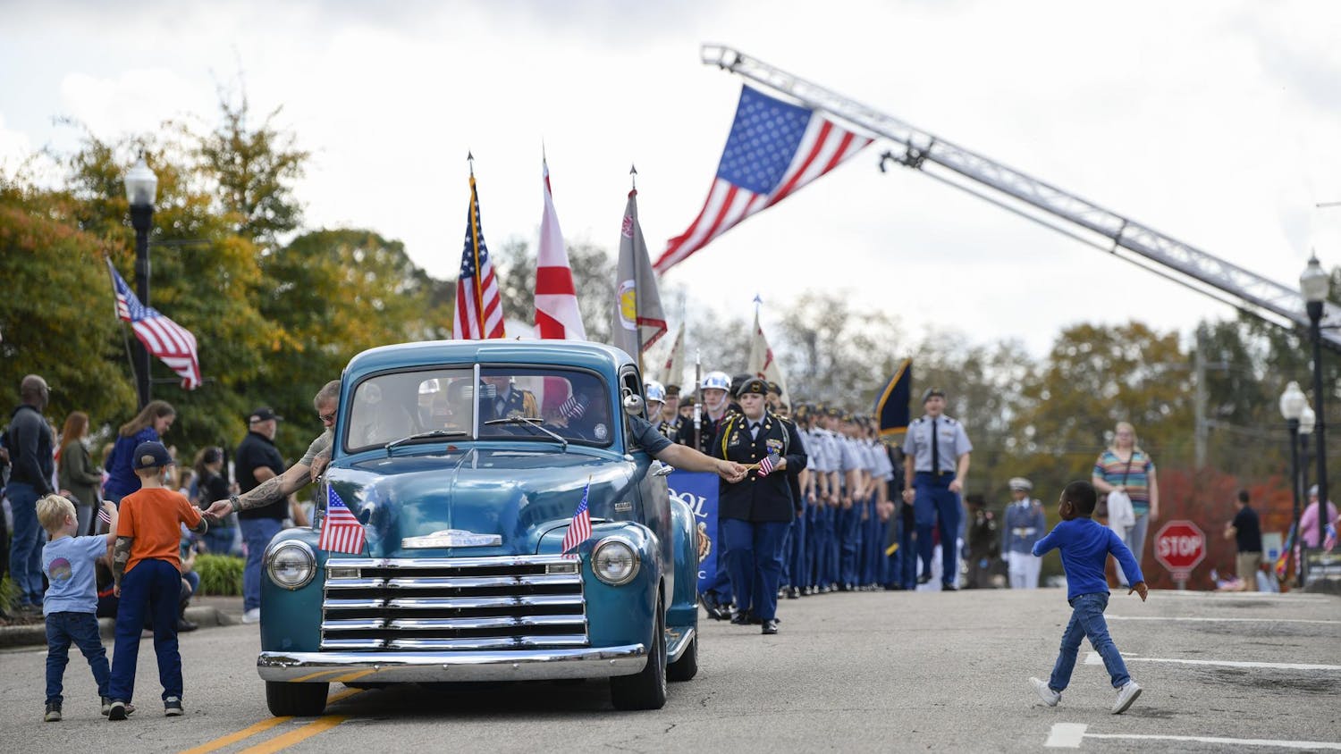 Children run to collect flags from a vintage car during the Freedom Fest Veterans Parade in Opelika, Ala., on Saturday, Nov. 8, 2025.