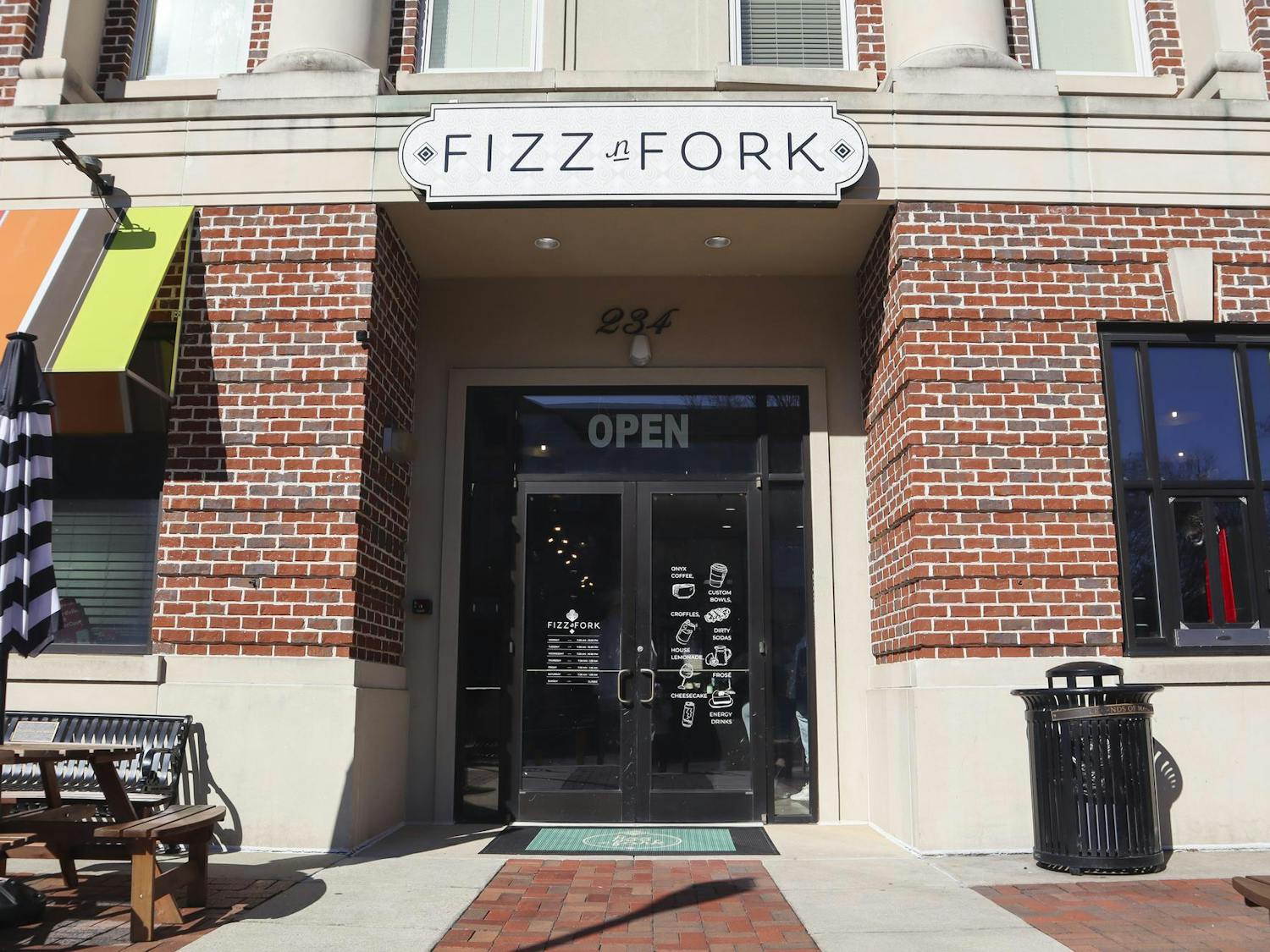 A brick storefront features a glass door with "OPEN" signage and a sign reading "FIZZ n FORK" above.