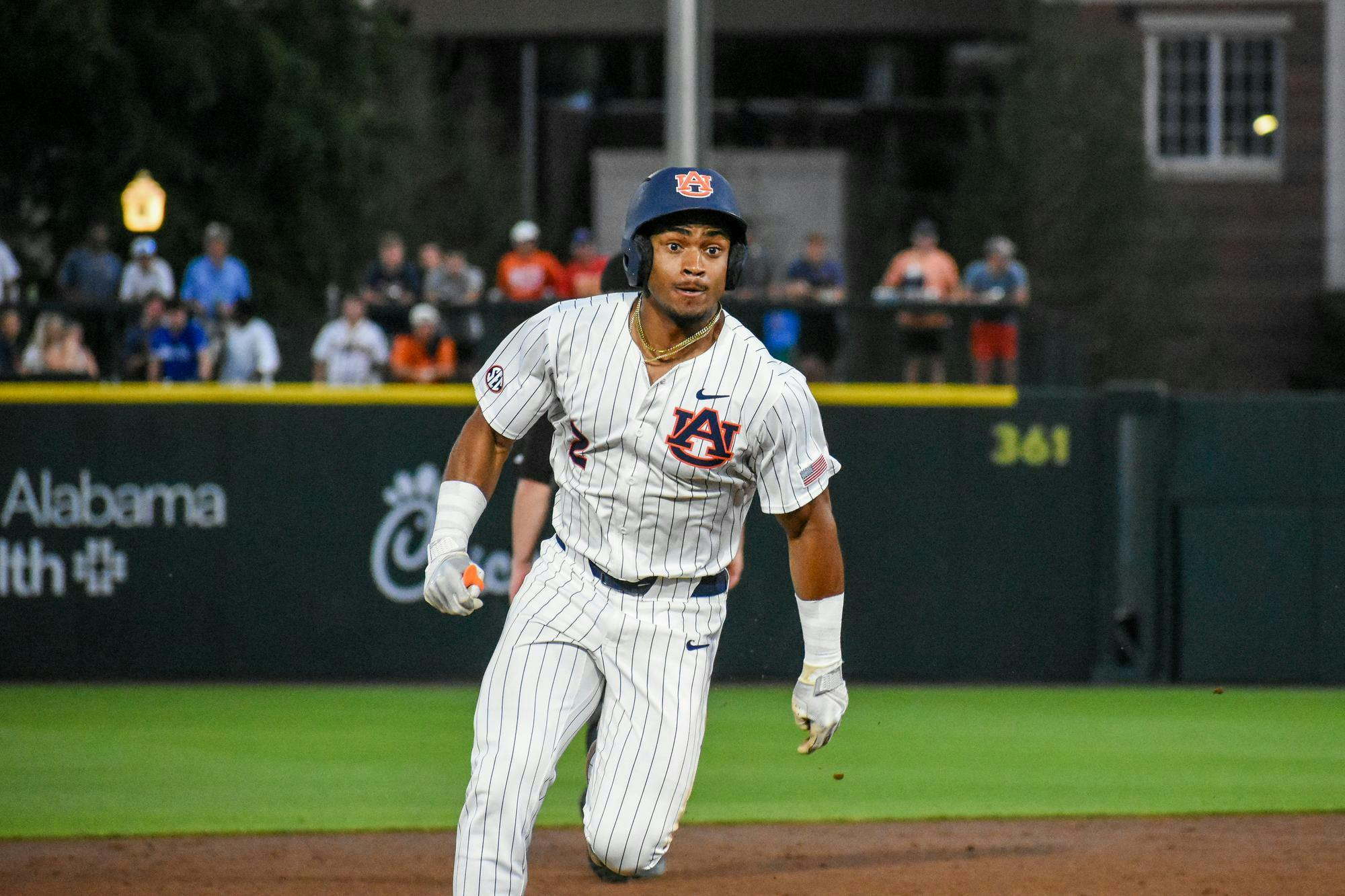 A baseball player in a striped uniform runs on the field, with spectators visible in the background.